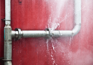 A burst water pipe against a red wall